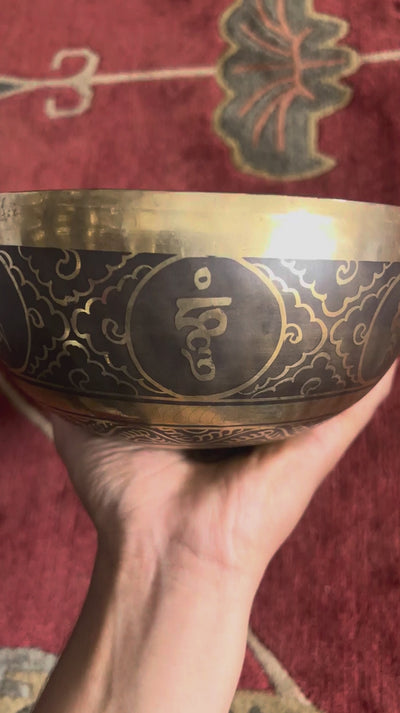 Conch shell engraved Tibetan singing bowl with dark bronze exterior and gold Tibetan script detailing.