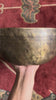 Tibetan singing bowl displaying a cosmic geometric pattern inside, with a wooden mallet and blue brocade cushion.