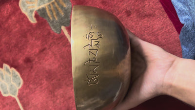 Side profile of a hand-hammered bronze Tibetan Moon singing bowl featuring a circular engraved auspicious emblem on a blue cushion.
