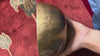 Side profile of a hand-hammered bronze Tibetan Moon singing bowl featuring a circular engraved auspicious emblem on a blue cushion.