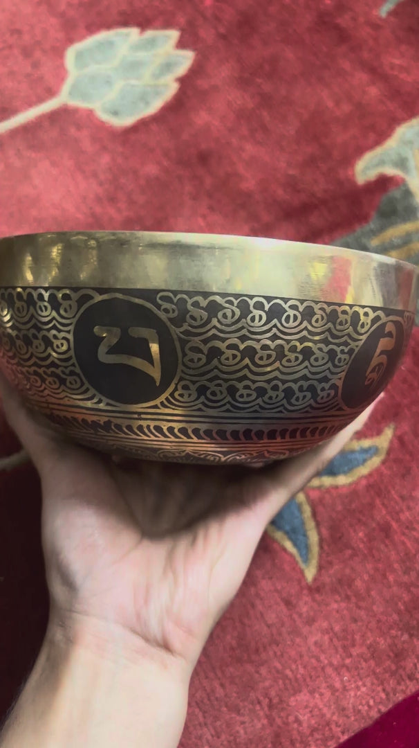 Load video: Engraved Endless Knot singing bowl displayed upright on a blue brocade cushion beside a wooden mallet, showing the central symbol and ornate interior borders.
