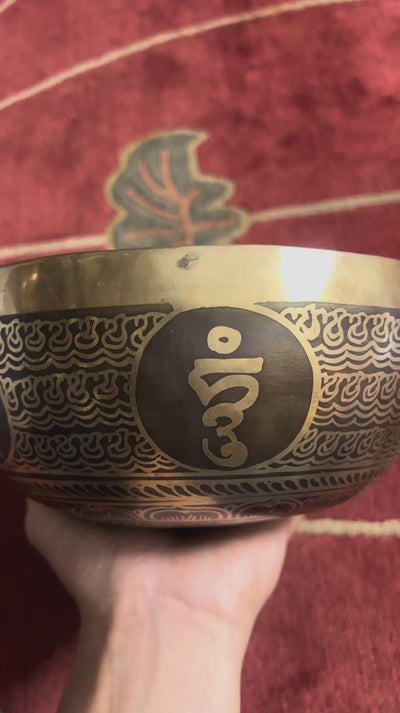 Flower of Life engraved Tibetan singing bowl displayed upright with a wooden mallet and blue brocade cushion.