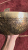 Golden and bronze Chengresi singing bowl featuring detailed floral engravings, displayed on a pink brocade cushion.