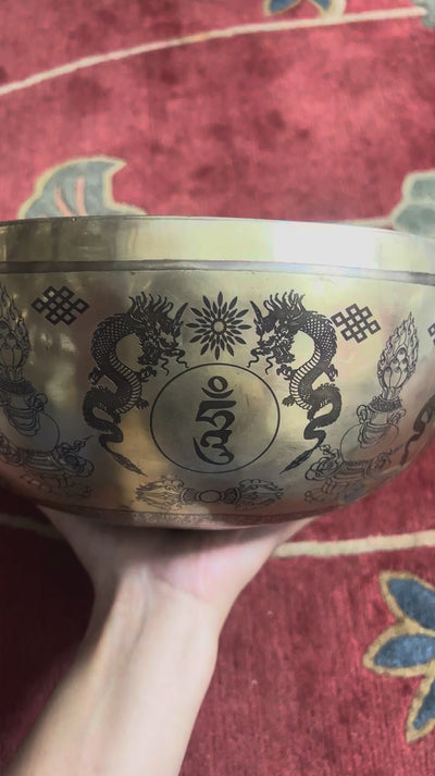 Green Tara bronze singing bowl displayed upright on a purple brocade cushion with two wooden handled mallets