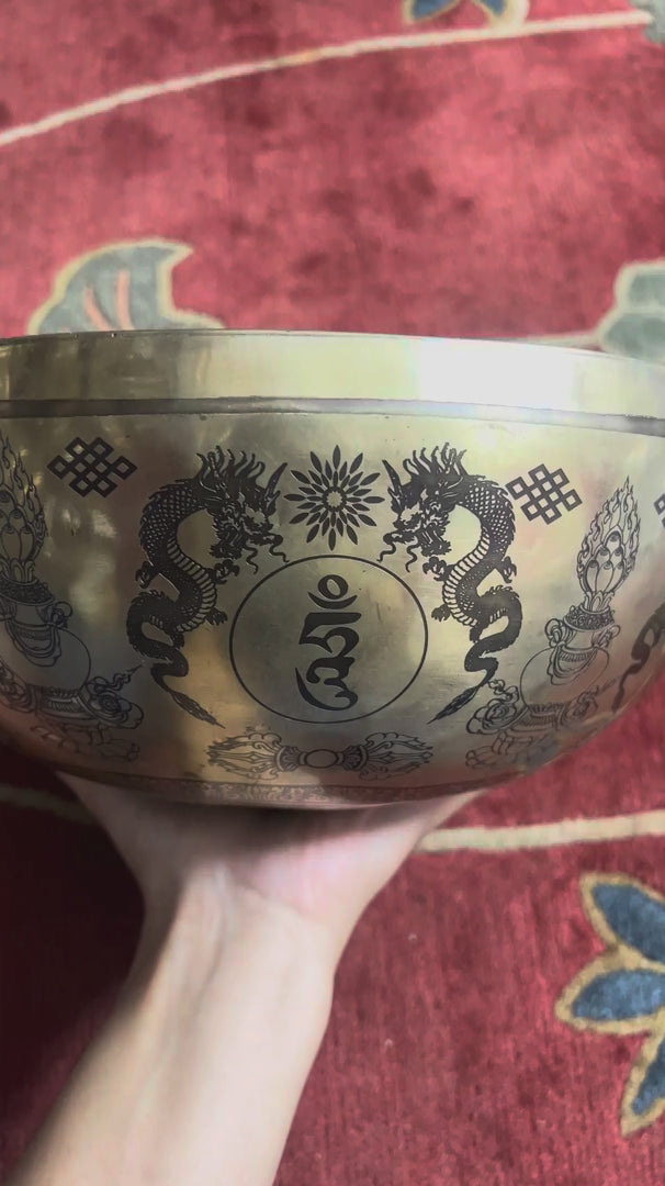 Load video: Green Tara bronze singing bowl displayed upright on a purple brocade cushion with two wooden handled mallets