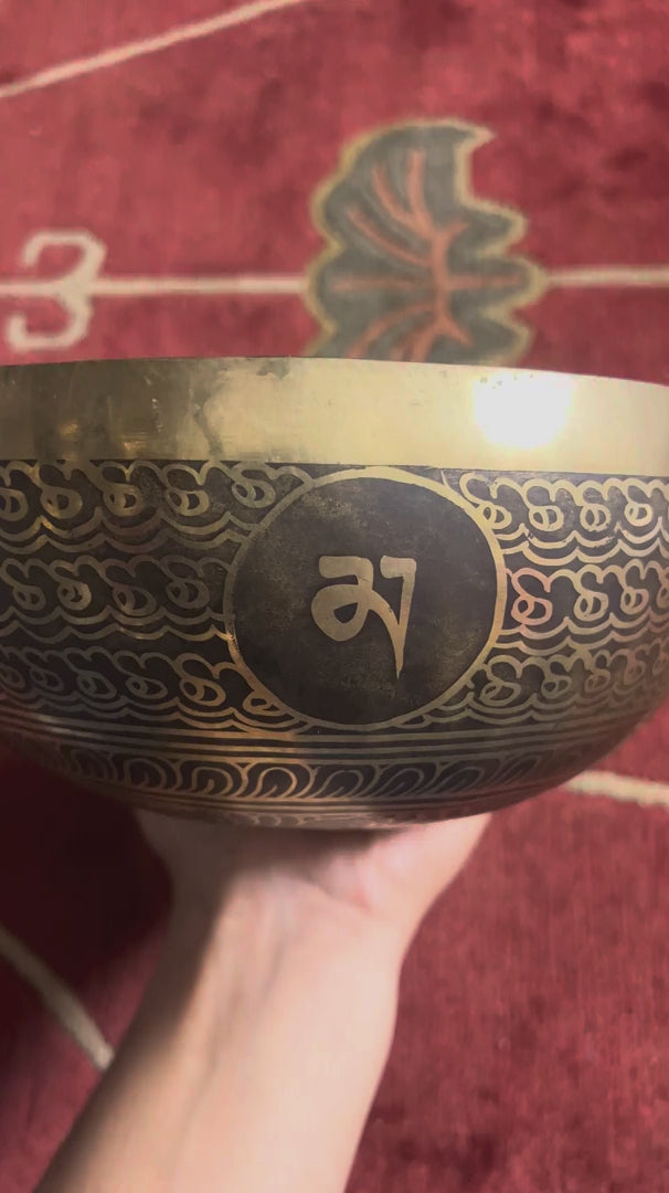 Engraved lotus singing bowl displayed upright with a wooden mallet and blue brocade cushion, showing the intricate golden lotus design inside.