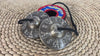 Tibetan Buddha tingsha cymbals featuring detailed Buddha engravings, a black connecting cord, and a colorful brocade carrying case.