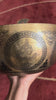 Buddha Mandala bronze singing bowl displayed upright on a purple brocade cushion with two mallets