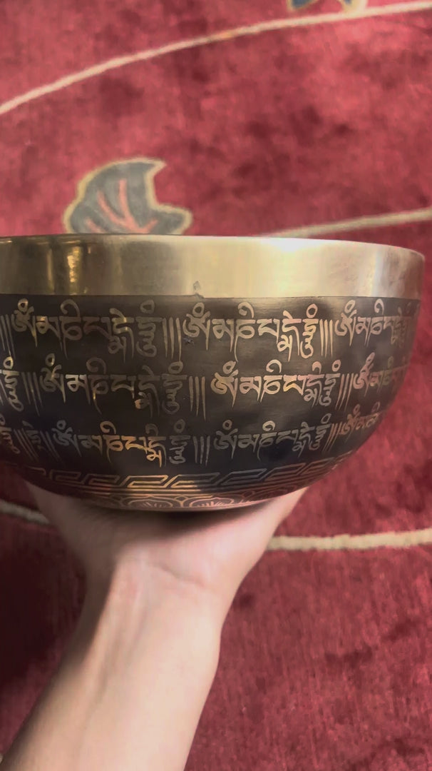 Load video: Close up inside a dark bronze Tibetan singing bowl showing a meditating yogi figure with seven hand-painted colored chakra symbols.