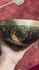Hindu Om singing bowl standing upright with a wooden mallet and blue brocade cushion, showing the central Om engraving.