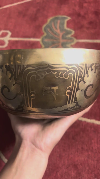 Hindu Om engraved singing bowl with dark decorative patterns and a blue brocade cushion on a woven mat.