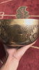 Hindu Om engraved singing bowl with dark decorative patterns and a blue brocade cushion on a woven mat.