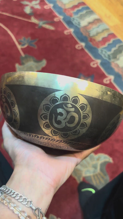 Handcrafted Om singing bowl from Nepal with golden Om engravings, dark bronze finish, decorative blue cushion and wooden striker.