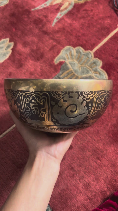 Ganesh singing bowl displayed upright with a wooden mallet and blue brocade cushion, showcasing its detailed interior engraving.