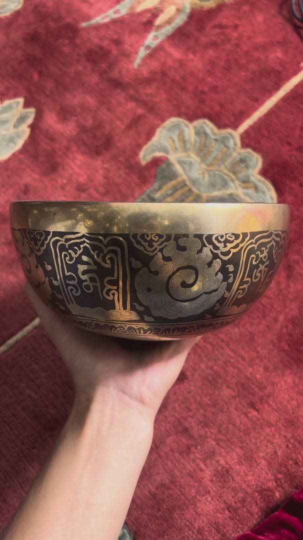 Load video: Ganesh singing bowl displayed upright with a wooden mallet and blue brocade cushion, showcasing its detailed interior engraving.