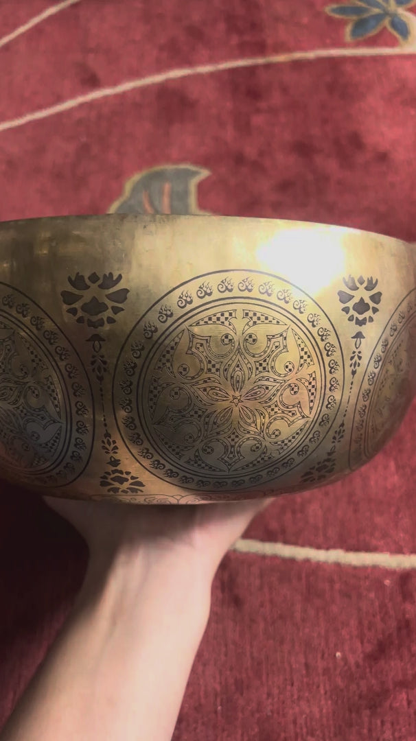 Avalokiteshvara singing bowl displayed upright with a wooden mallet and red felt mallet, showing intricate Buddhist engravings.