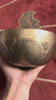 Engraved Kal Mandala singing bowl shown upright with a wooden mallet and decorative cushion.