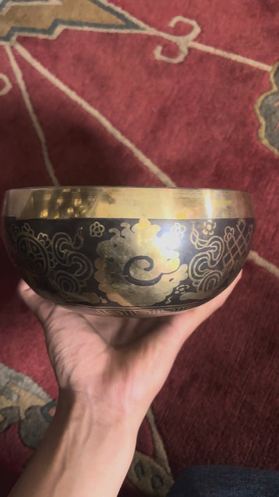 Buddha Eye singing bowl displaying engraved Wisdom Eyes inside the bowl with a wooden mallet and blue brocade cushion.