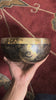 Buddha Eye singing bowl displaying engraved Wisdom Eyes inside the bowl with a wooden mallet and blue brocade cushion.