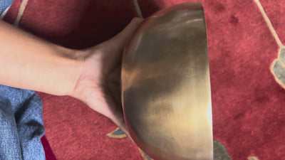 Side view of a classic plain hand-hammered bronze Tibetan singing bowl resting on a blue brocade cushion.