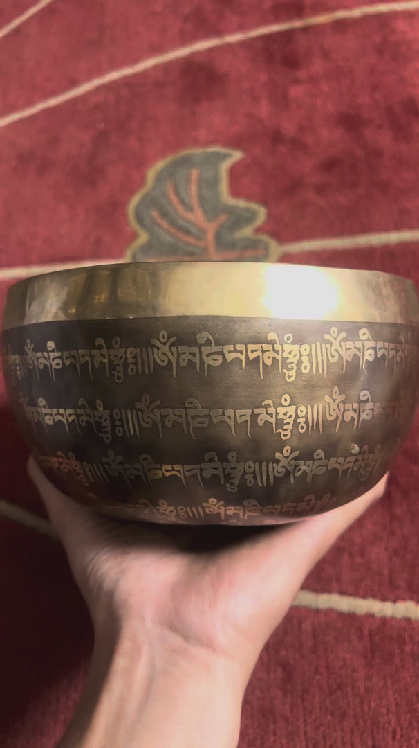 Load video: Singing bowl displayed upright with a wooden mallet and blue brocade cushion, showing the central Flower of Life geometric pattern and Tibetan script.