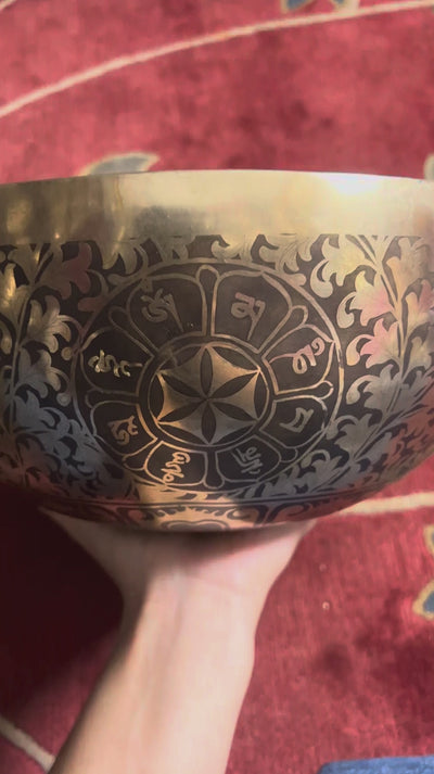 Golden and dark bronze Chakra Manab Tibetan singing bowl with intricate floral and geometric engravings displayed on a pink brocade cushion.