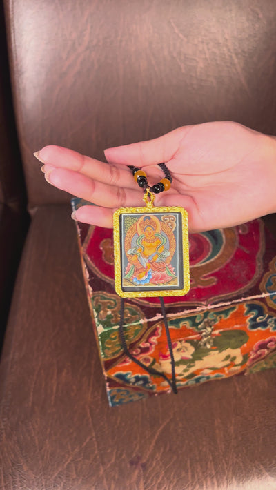 Hand-painted Zambala miniature Thangka pendant in gold-accented copper Ghau locket displayed hanging from black beaded cord.