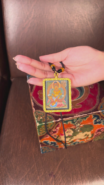 Hand-painted Zambala miniature Thangka pendant in gold-accented copper Ghau locket displayed hanging from black beaded cord.