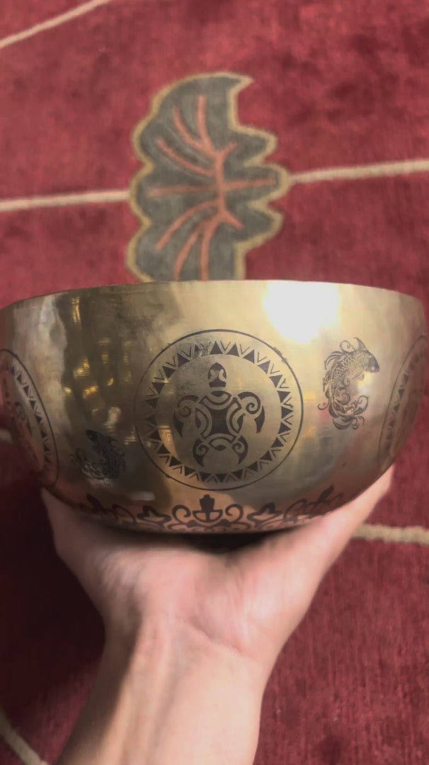 Load video: Turtle inspired engraved singing bowl displayed upright with a wooden mallet and blue cushion, showing the detailed interior artwork.